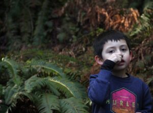 A child holds a crushed California bay leaf up to their nose.